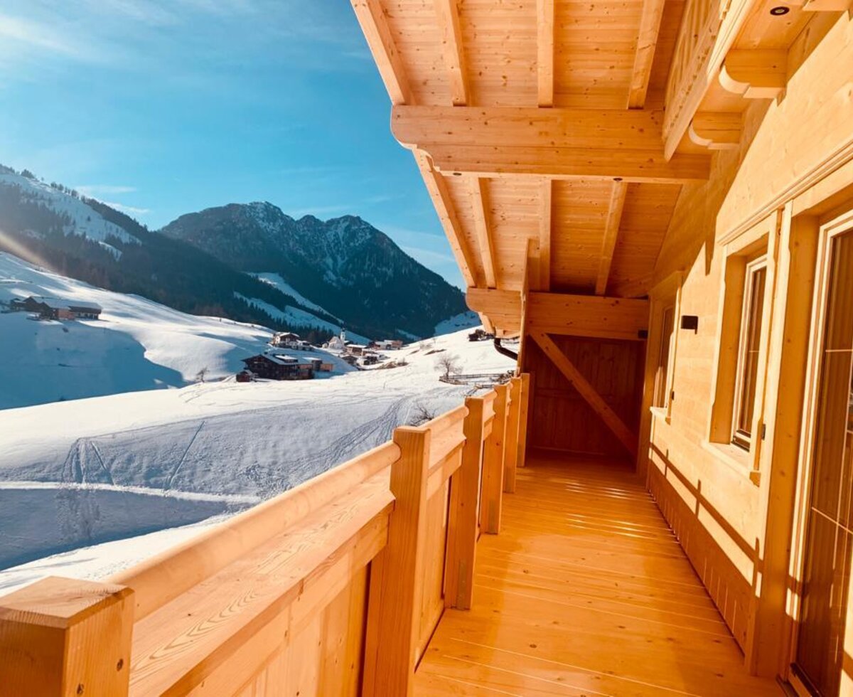 Heller Holzbalkon des Bauernhofs mit direktem Zugang und Blick auf die verschneite Berglandschaft.