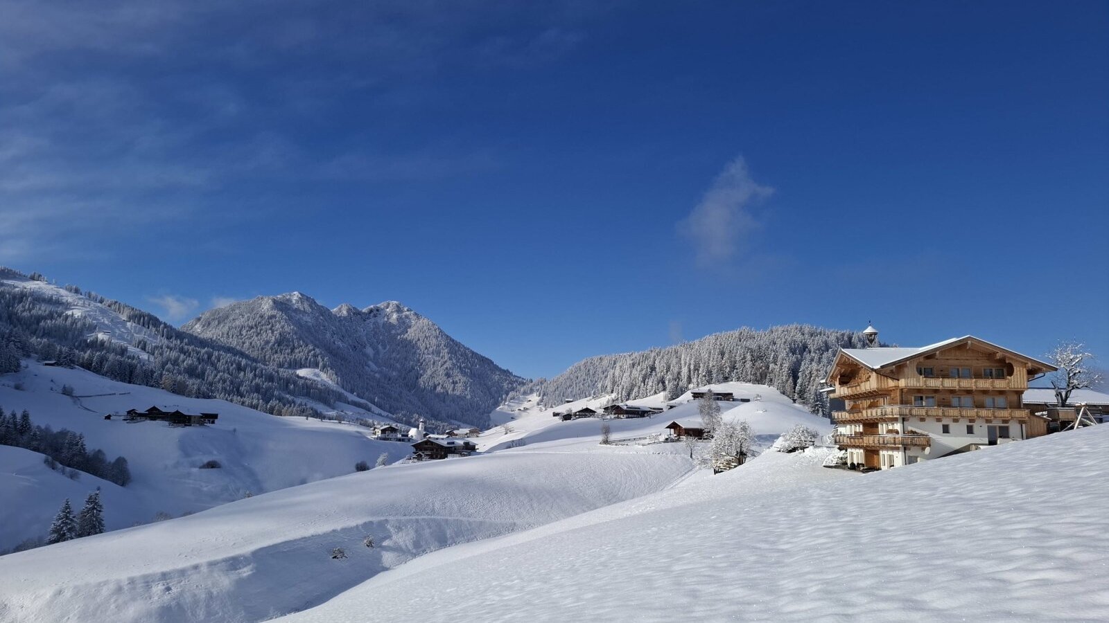 SonnenAppartments verschneit mit Dorf Thierbach unter blauem Himmel.