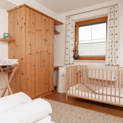 Zimmer im Bauernhof mit Babybett, Wickeltisch und Holzkleiderschrank.