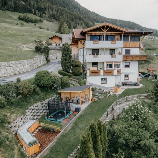 Der Bauernhof verfügt über ein mehrstöckiges Gebäude mit Balkonen, einem Gartenbereich mit Trampolin, einer Holzpergola und einem Kinderspielplatz.