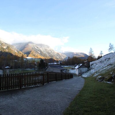 Die Berglandschaft rund um den Bauernhof mit einem Weg, Gebäuden und Schneeresten an den Hängen.