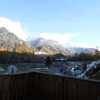 Blick vom Balkon des Bauernhofs auf das Tal mit Bergen, Herbstbäumen und einem Dorf.