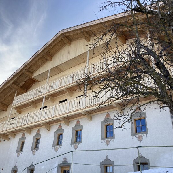 Außenansicht des Bauernhofs mit traditionellen Holzbalkonen und dekorativer Fassadenmalerei.