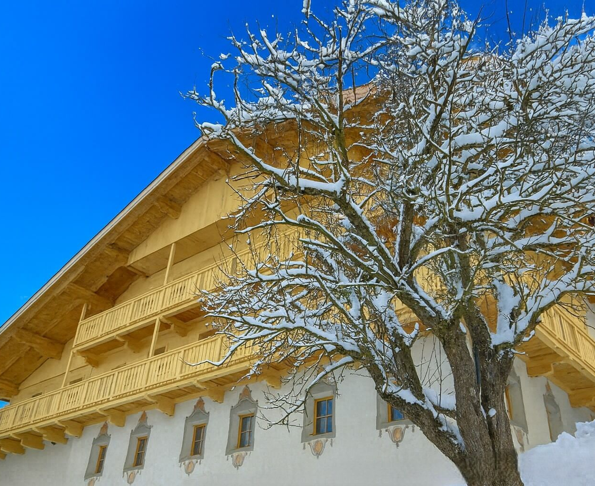 Der verschneite Bauernhof mit seinen Holzbalkonen und der traditionellen Fassade im Winter.