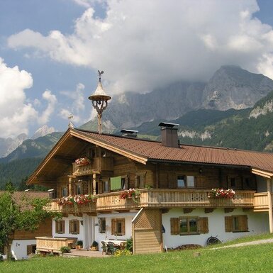 Der Bauernhof mit Holzfassade, blumengeschmückten Balkonen und Bergblick.