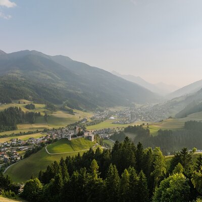 Blick auf das Tal mit einem Ort und einer Burg, umgeben von Bergen und Wäldern.