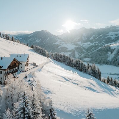 Der Bauernhof in einer verschneiten Berglandschaft unter strahlendem Sonnenschein.