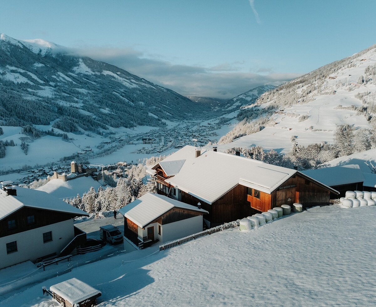 Der Bauernhof im Winter, umgeben von Schnee und Bergen, mit Blick auf das Tal.