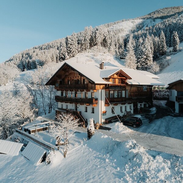 Der Bauernhof im Winter mit Balkonen und einem Kinderspielplatz auf der Terrasse, umgeben von verschneiten Bergen.
