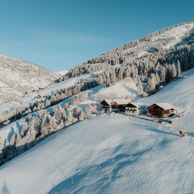 Der Bauernhof in einer verschneiten Berglandschaft, umgeben von Wäldern.