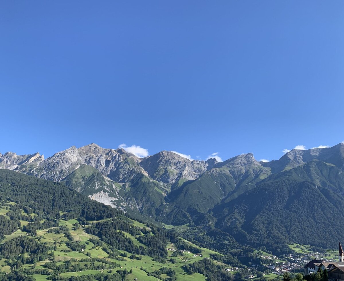 Blick auf die Berge, bewaldete Hänge und ein Tal mit einem Dorf vom Bauernhof aus.