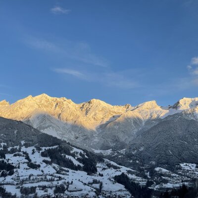Blick auf die schneebedeckten Berge und das Tal mit einem Dorf vom Bauernhof aus.