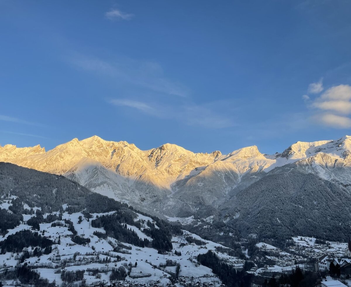 Blick auf die schneebedeckten Berge und das Tal mit einem Dorf vom Bauernhof aus.