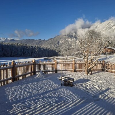 Der verschneite Gartenbereich des Appartements "d´kloane Mühle" mit Feuerschale und Blick auf die umliegende Berglandschaft.
