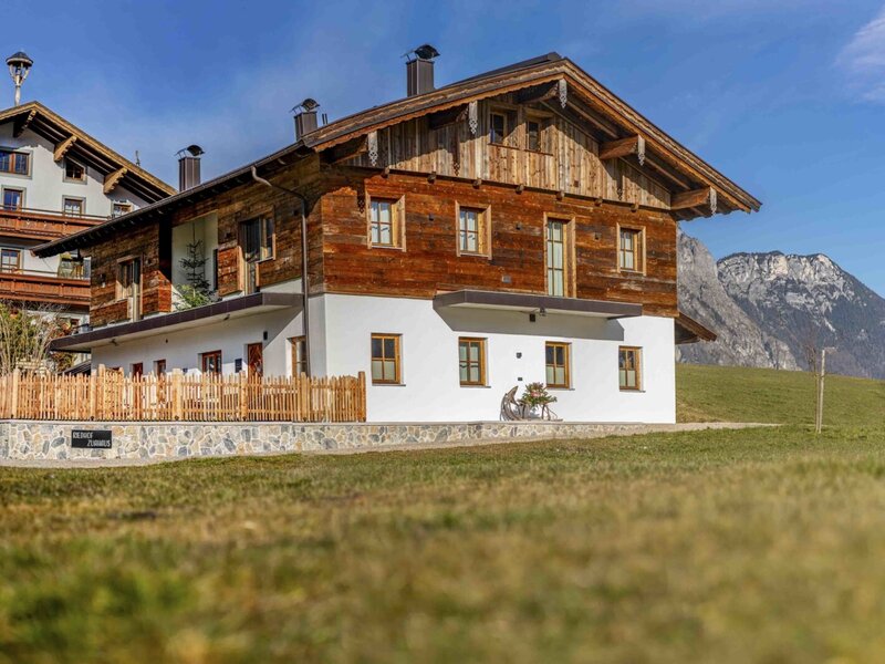 Außenansicht des Zuahaus auf dem Bauernhof mit traditioneller Holzfassade, weißem Untergeschoss und Bergblick.