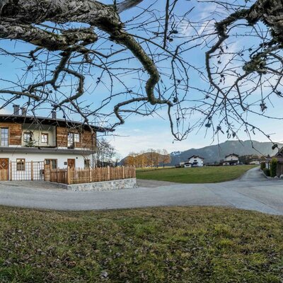 Außenansicht des Bauernhofs 'Zuahaus' mit weißer Fassade, Holzverkleidung und der umliegenden Berglandschaft.