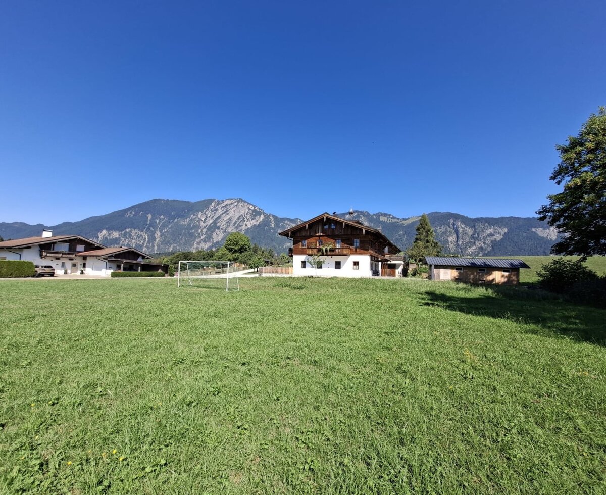 Der einladende Bauernhof mit einer weitläufigen grünen Wiese, einem Fußballtor und einer malerischen Bergkulisse im Hintergrund.