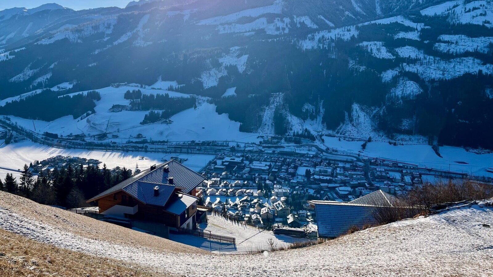 Blick vom Bauernhof auf die schneebedeckte Berglandschaft und das Tal mit dem Dorf.
