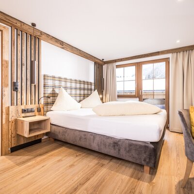 Schlafbereich im Bauernhof mit Doppelbett, Holzelementen, Zugang zum Essbereich und einem Fenster mit Blick auf die Landschaft.