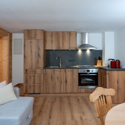 Moderne Küche in den Ap­par­te­ments mit Holzschränken, Spüle, Herd und Backofen, offen zum Wohnbereich.
