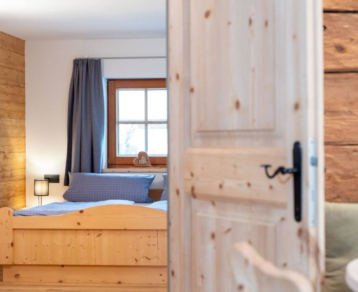 Schlafzimmer im Ap­par­te­ment mit Holzbett, Fenster und Holzwand.