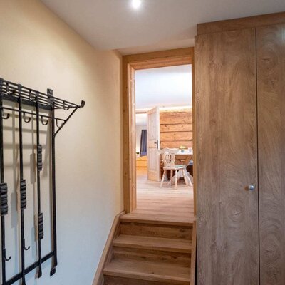Eingangsbereich des Ap­par­te­ments mit Holztreppe, Garderobe und integriertem Schrank, mit Blick in den Wohnbereich.