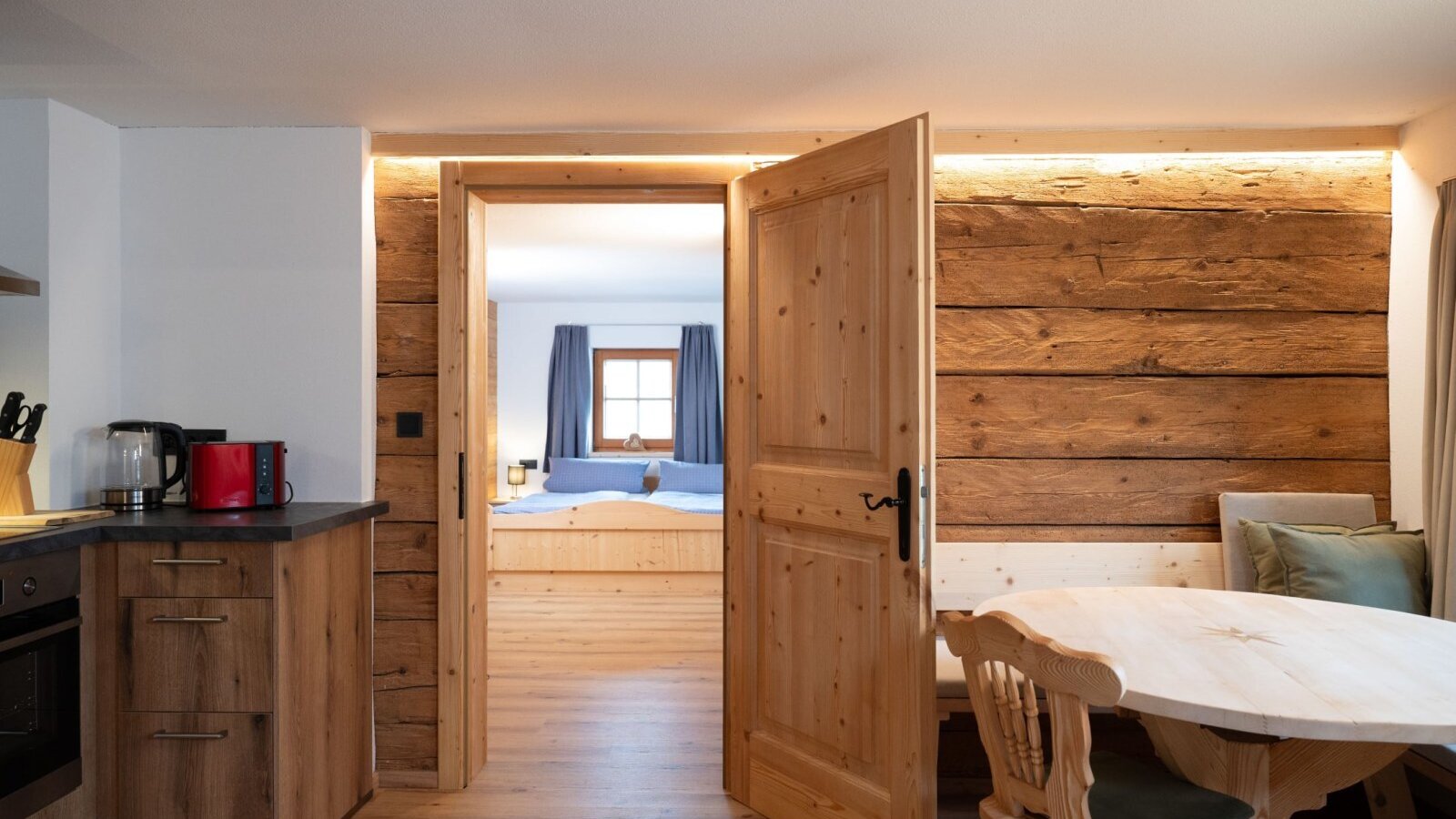 Küchen- und Essbereich des Ap­par­te­ments mit Holzeinrichtung und Zugang zu einem Schlafzimmer.