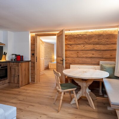 Küche und Essbereich des Ap­par­te­ments mit moderner Ausstattung, Backofen und Holztisch mit Eckbank.