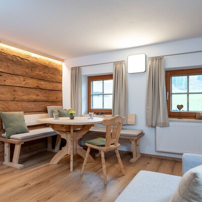 Wohn- und Essbereich des Ap­par­te­ments mit Holztisch, Eckbank und zwei Fenstern.