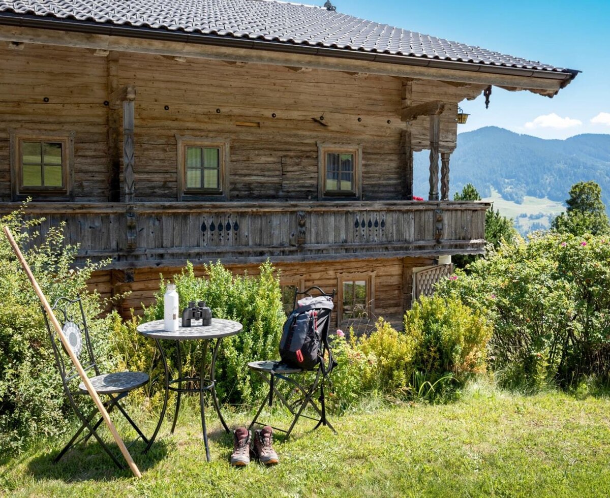 Die idyllische Außenseite des Bauernhofs mit einer gemütlichen Sitzecke im Grünen und malerischem Blick auf die Berge.