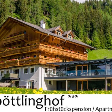 Der Bauernhof kombiniert ein traditionelles Holzgebäude mit mehreren blumengeschmückten Balkonen und einen modernen Anbau mit großen Fensterfronten vor bewaldeten Hügeln.