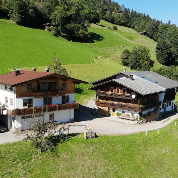 Der Bauernhof mit zwei Gebäuden und grünen Hügeln, inklusive einer Saunahütte auf der Terrasse des linken Hauses.