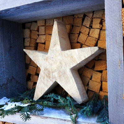 Hölzerner Stern als Dekoration im Holzstapel des Bauernhofs, mit Tannenzweigen und Schnee.