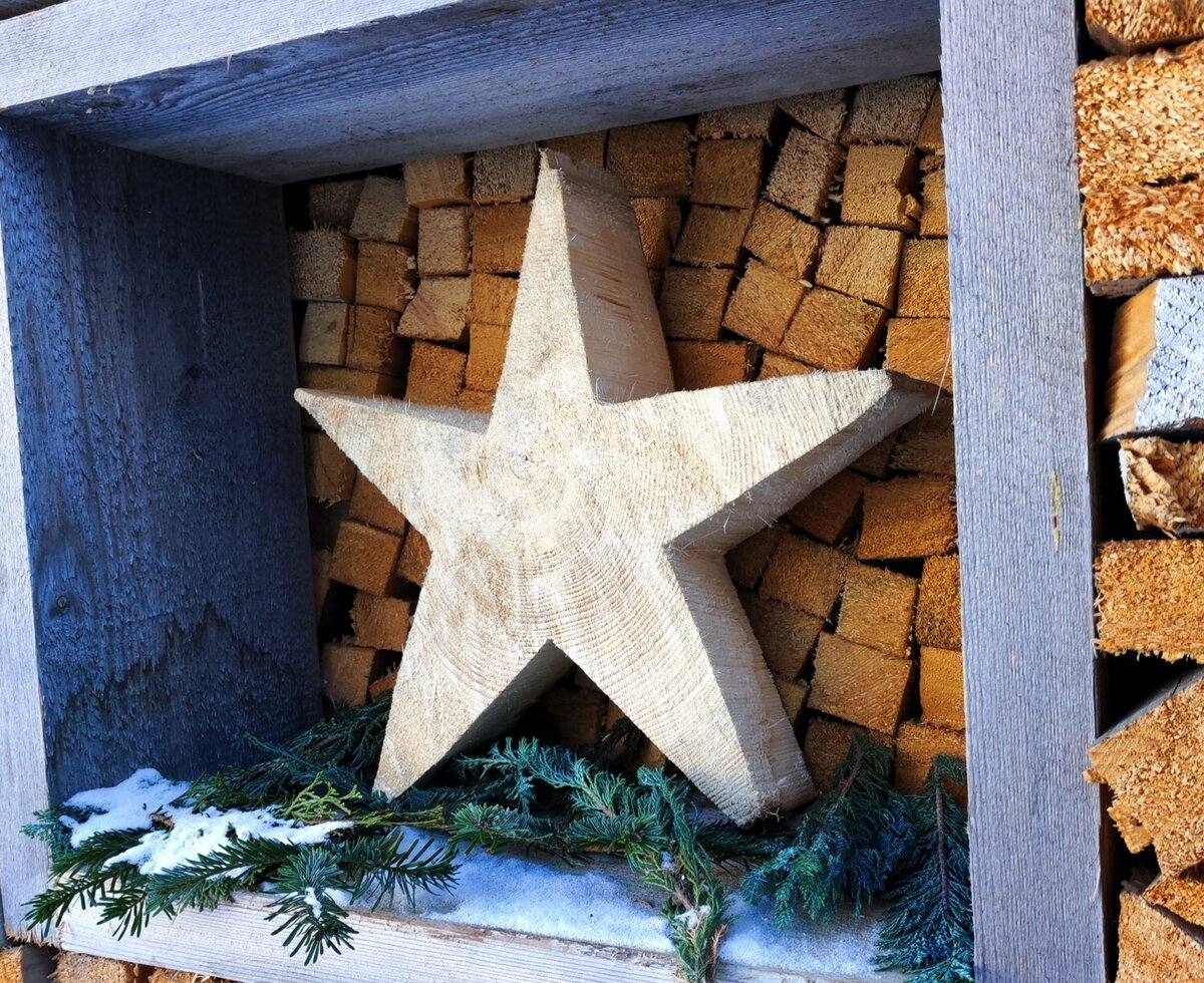 Hölzerner Stern als Dekoration im Holzstapel des Bauernhofs, mit Tannenzweigen und Schnee.
