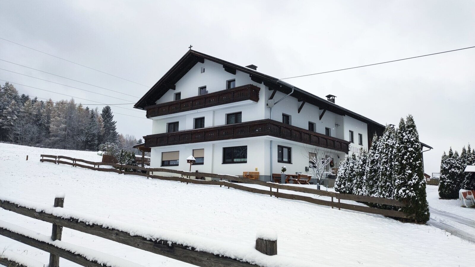 Außenansicht des Bauernhofs im Winter, umgeben von Schnee und einem Holzzaun.
