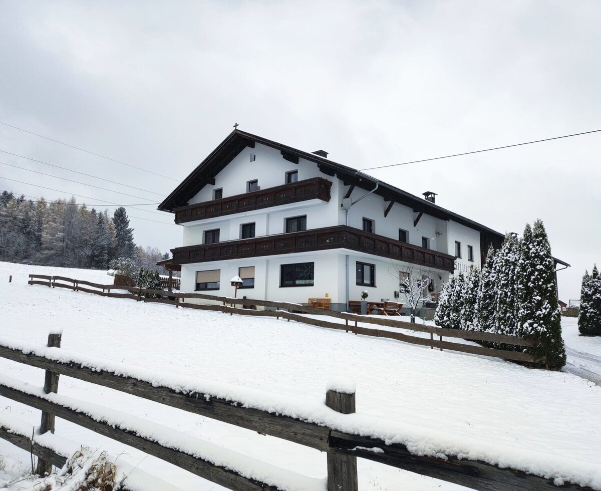 Außenansicht des Bauernhofs im Winter, umgeben von Schnee und einem Holzzaun.