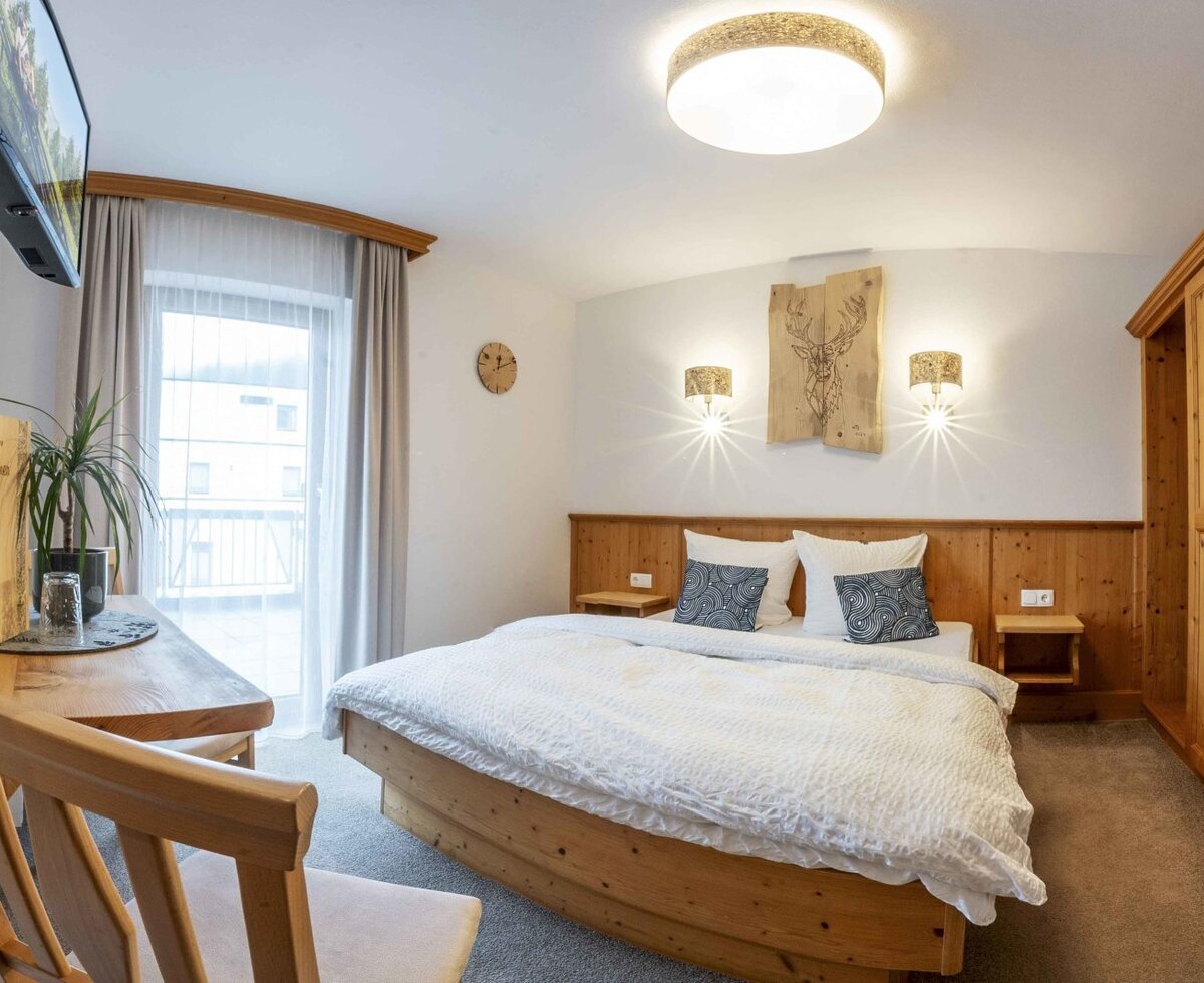 Doppelzimmer im Bauernhof mit Holzbett, Wandfernseher, Kleiderschrank, Schreibtisch und Zugang zum Balkon.
