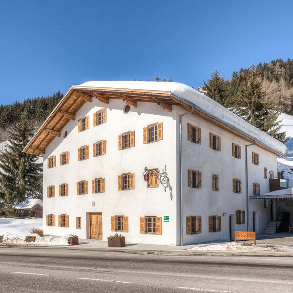 Außenansicht des Bauernhofs mit weißer Fassade, Holzfensterläden und schneebedecktem Dach.