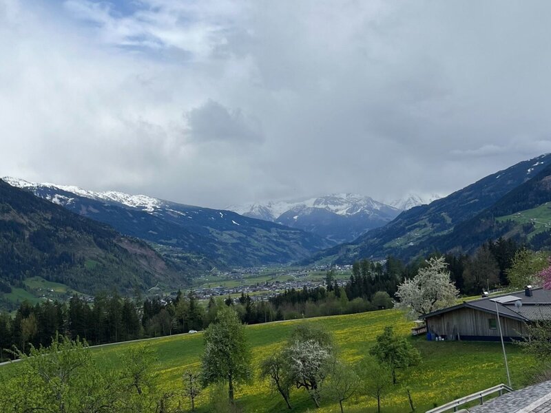 Blick vom Bauernhof auf das Tal mit schneebedeckten Bergen und einem Dorf.