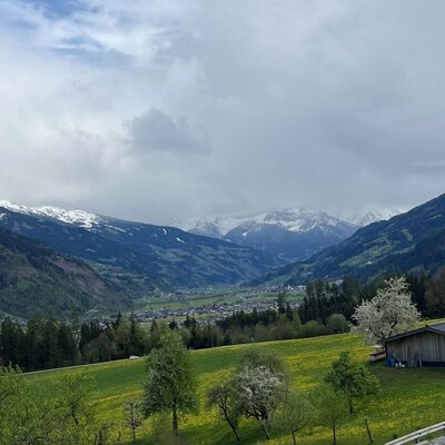 Blick vom Bauernhof auf das Tal mit schneebedeckten Bergen und einem Dorf.