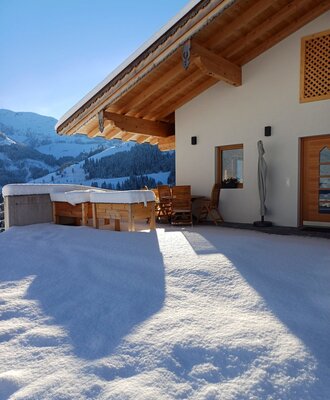 Die verschneite Terrasse der Ferienwohnung mit Gartenmöbeln und Blick auf die winterliche Berglandschaft.