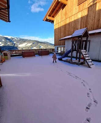 Der verschneite Außenbereich des Bauernhofs mit Kinderspielplatz und Bergblick.