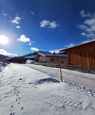 Der idyllische Bauernhof inmitten einer verschneiten Winterlandschaft unter strahlend blauem Himmel.