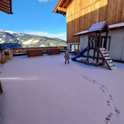 Der verschneite Außenbereich des Bauernhofs mit Kinderspielplatz und Bergblick.