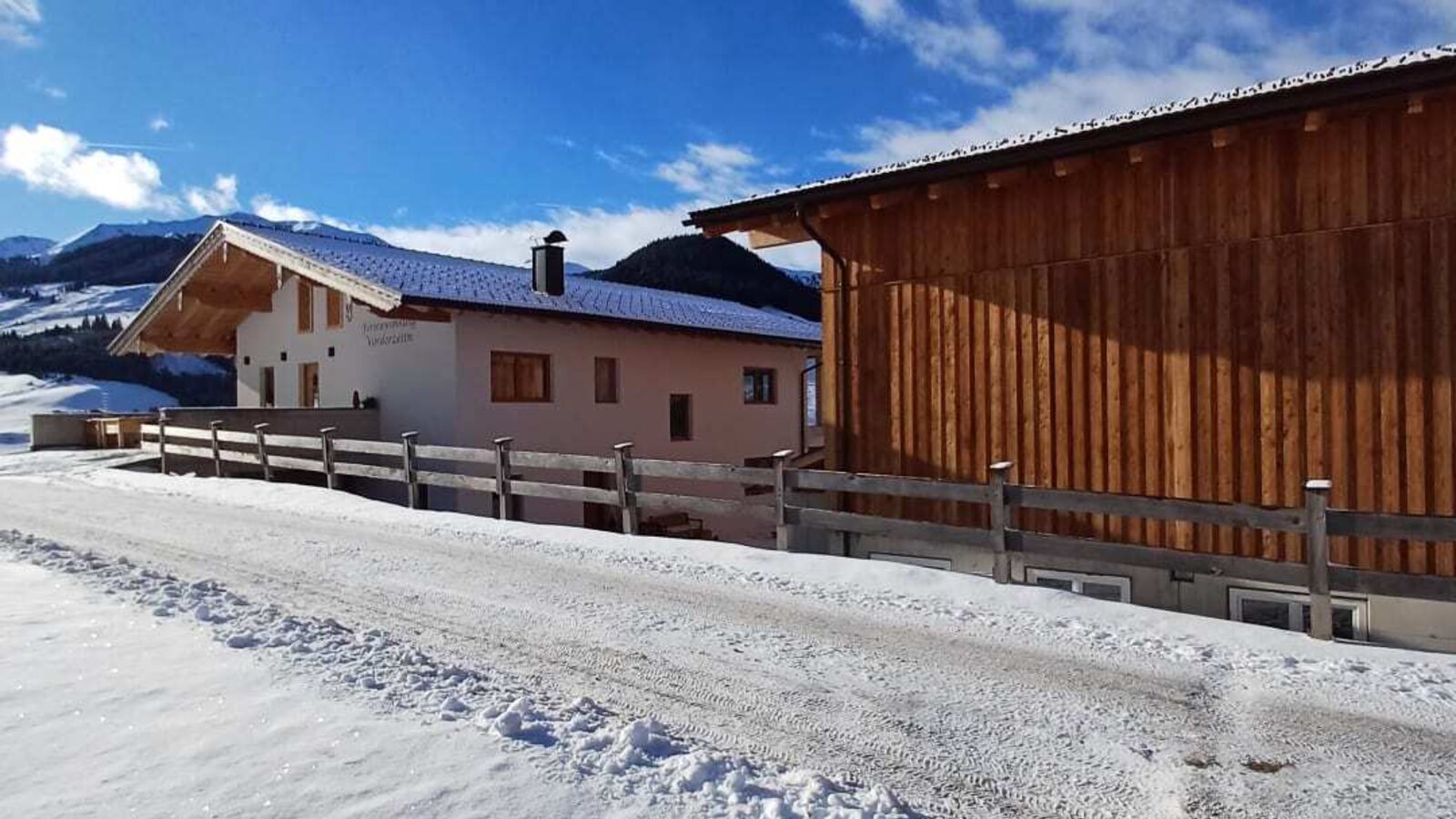 Der Bauernhof im Winter, mit verschneiter Zufahrt und einem Holzgebäude.