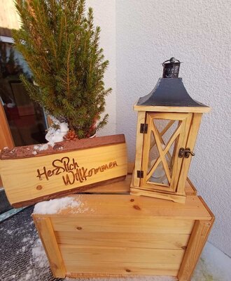 Ein einladender Gruß am Eingang des Bauernhofs mit einem rustikalen Holzschild, einer Laterne und winterlicher Dekoration.