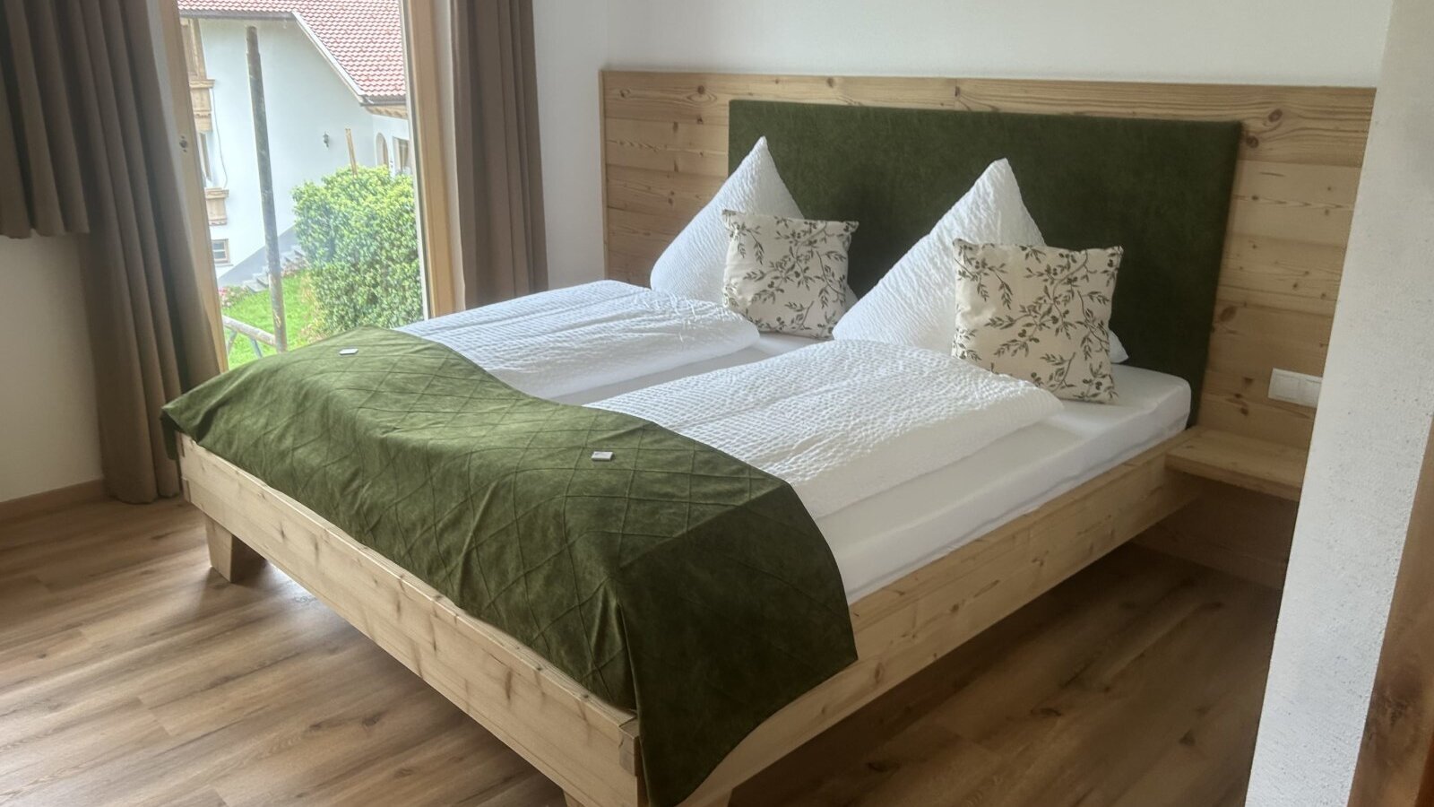 Doppelzimmer im Bauernhof mit Holzbett, grünem Kopfteil und Fenster.
