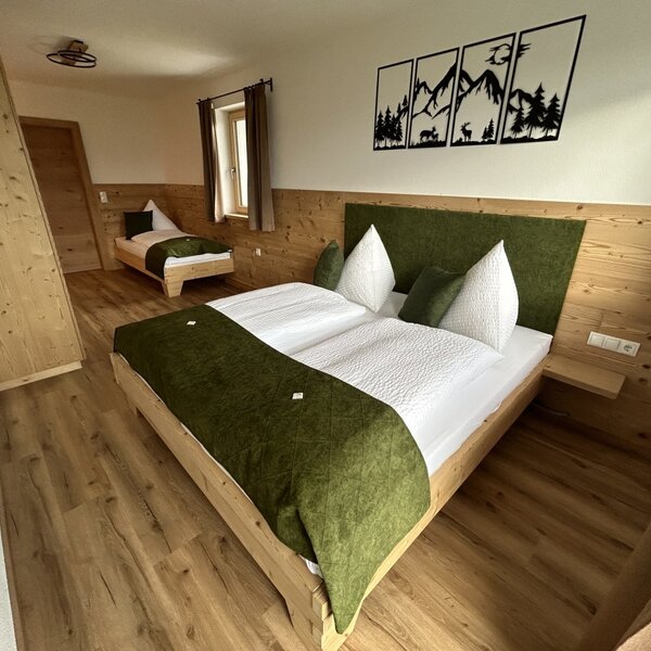 Schlafzimmer im Bauernhof mit einem Doppelbett und einem Einzelbett, eingerichtet mit Holzmöbeln und Wandpaneelen.