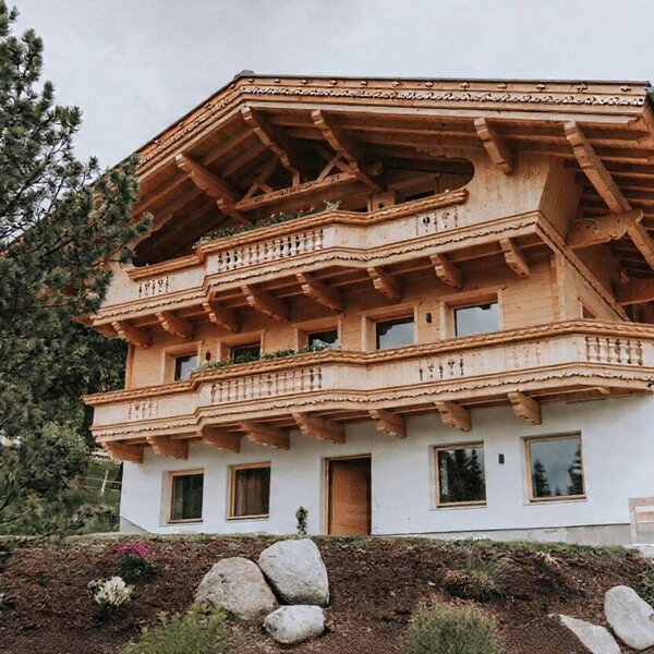 Außenansicht des Bauernhofs mit mehreren Etagen, Holzbalkonen und weißer Fassade.
