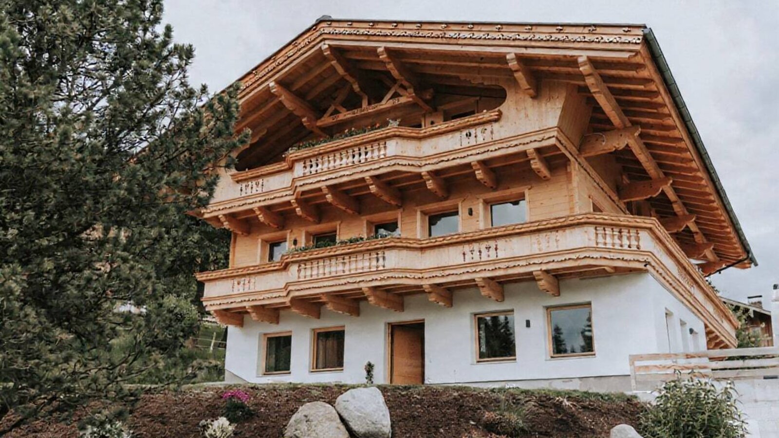 Außenansicht des Bauernhofs mit mehreren Etagen, Holzbalkonen und weißer Fassade.